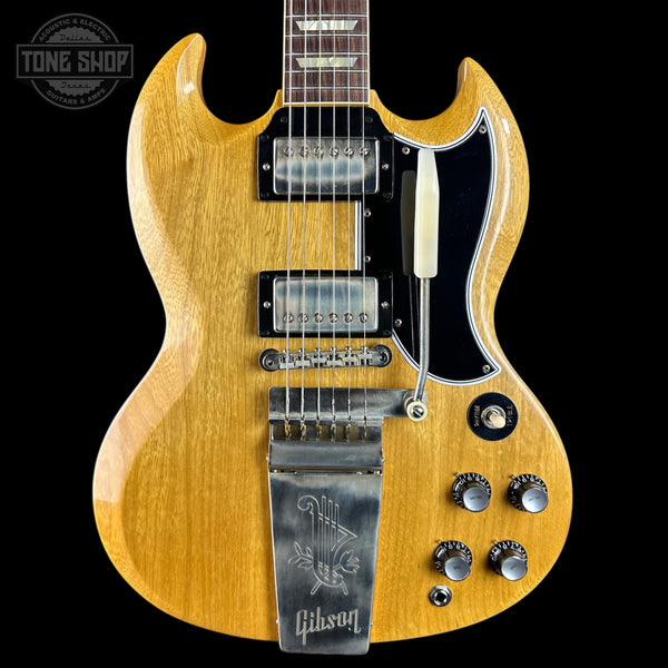 A Gibson SG electric guitar in a natural wood finish with a black pickguard, dual humbucker pickups, and a chrome tailpiece, shown against a solid black background with a Tone Shop watermark in the top left corner.