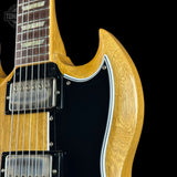 Close-up of a double-cutaway electric guitar body with a natural wood finish, black pickguard, and chrome hardware against a black background.