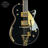 Black electric guitar with gold hardware on a black background, featuring 'Tone Shop' branding.
