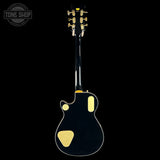 Black electric guitar with gold hardware on a black background, featuring the Tone Shop logo.