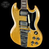 A Gibson SG electric guitar in a natural wood finish, shown from the side against a solid black background. The guitar features a glossy natural wood body, a black pickguard, dual humbucker pickups, and a chrome tailpiece.