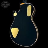 Black electric guitar with gold hardware on a black background, featuring 'Tone Shop' logo.