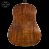 Back view of a wooden acoustic guitar with a visible brand logo in the corner.