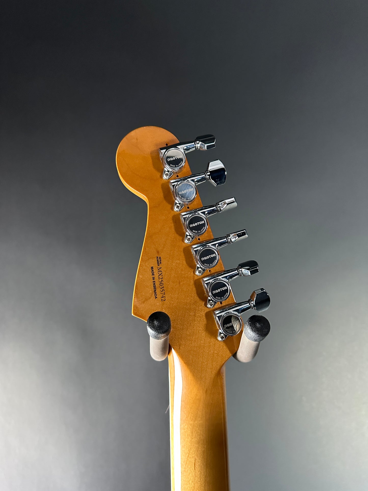 Close-up of a guitar headstock with tuning pegs on a gray background