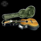 An acoustic guitar with a natural wood body and dark headstock, displayed inside an open black hard case with green velvet lining, set against a solid black background. A 'TONE SHOP' watermark is visible in the top-left corner.