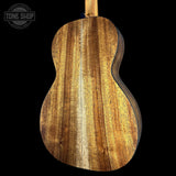 Close-up of the back of a wooden acoustic guitar showing the natural wood grain finish, set against a solid black background with a Tone Shop watermark in the top left corner.