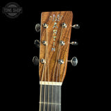 Close-up of the headstock of a Martin acoustic guitar, showing the wood grain, six tuning pegs, and six strings against a solid black background.