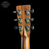 Close-up of the headstock of a wooden acoustic guitar against a solid black background, showing six tuning pegs with decorative metal caps and a Tone Shop watermark in the upper left corner.