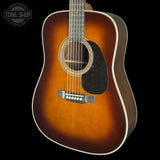 A classic acoustic guitar with a sunburst finish, featuring a warm brown center fading to black around the edges, a dark pickguard, and a white binding, shown against a solid black background.