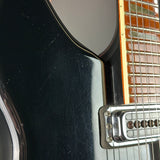 Close-up of a black electric guitar with a pickguard and part of the neck.