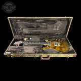 An electric guitar with a gold-toned flamed maple top and black headstock, displayed inside an open vintage-style hard case with a distressed gold and black patterned exterior and dark gray velvet interior. A 'TONE SHOP' logo watermark is visible in the top left corner.