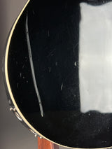Close-up of a black guitar's soundhole with visible scratches and a drop of water.