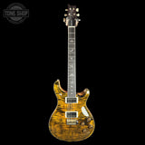 A classic electric guitar with a vibrant yellow-orange flame maple wood finish, shown against a solid black background. The brand is identifiable as aPRS due to the distinctive body shape, headstock, and hardware design.