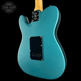 Teal electric guitar with a black pickguard on a black background, featuring 'Tone Shop' branding.