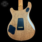 Close-up of the back of an electric guitar body with a natural wood finish, black pickguard, and a light blue flame finish accent on the right side, shown against a black background.