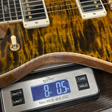 Close-up of a guitar body resting on a digital scale to show weight, with the scale displaying 8.05 oz.