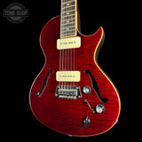 Red electric guitar with a black background, featuring the Tone Shop logo.