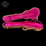 An open guitar or bass guitar case with a bright pink velvet interior and tan leather exterior, photographed against a solid black background. A Tone Shop watermark is visible in the top-left corner.