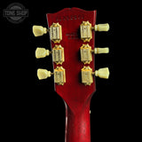 Close-up of the headstock of a red acoustic guitar, showing six gold tuning pegs and white tuning keys against a black background.