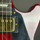 Close-up detail of an electric guitar body showing a red-flecked white pickguard, gold humbucker pickups, and gold screws on a dark gray background.