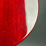 Close-up of a glossy red wooden object with visible wood grain and a few scratches on a gray background.