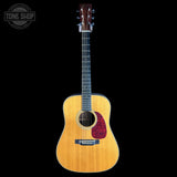 A natural wood acoustic guitar with a dark red pickguard, shown vertically against a solid black background. A Tone Shop watermark is visible in the top-left corner.