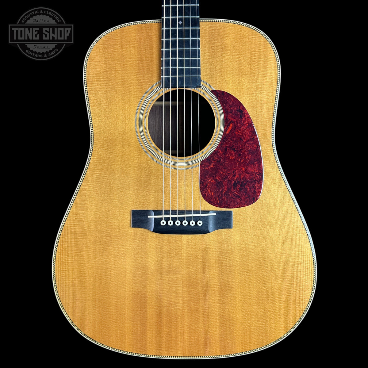 A front-facing acoustic guitar with a natural flamed maple top, dark fretboard, and a red marbled pickguard, shown against a solid black background with a Tone Shop watermark in the upper left.