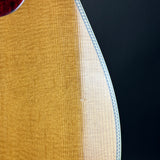 Close-up detail of an acoustic guitar body showing the natural wood grain, sound hole surround, and decorative white inlay against a dark background.