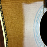 Close-up detail of an acoustic guitar body showing the natural wood grain top, sound hole rosette, and part of the dark wooden side.