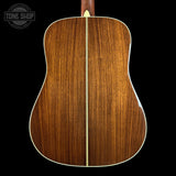 The back of an acoustic guitar made of rich brown wood with a single light-colored center stripe, shown against a solid black background with a Tone Shop watermark in the top left.