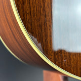 Close-up of a wooden acoustic guitar body showing the glossy brown wood grain, a light cream binding edge, and a small patch of worn or damaged finish near the lower edge.