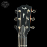 Close-up of a Taylor acoustic guitar headstock against a black background, showing six silver tuning pegs, strings, and the Taylor logo.
