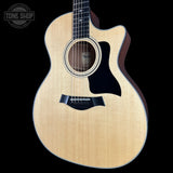 A Taylor acoustic-electric guitar with a natural flamed maple top and dark sides, shown against a solid black background with a Tone Shop watermark in the top-left corner.
