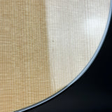 Close-up detail of a guitar body showing the natural wood grain finish and the edge of the soundhole rim against a dark background.