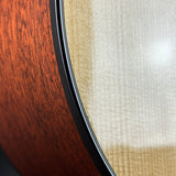 Close-up detail of a guitar body showing the reddish-brown wood veneer on the left, a light natural wood back, and a black edge trim.