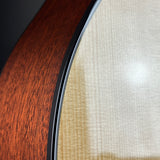 Close-up detail of an acoustic guitar showing the rich reddish-brown wood body on the left and the light natural wood top on the right, separated by a black edge.
