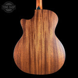 Close-up of the back of an acoustic guitar showing a rich, warm brown wood grain finish, with a black background and a Tone Shop watermark in the top left corner.