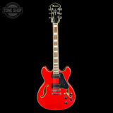 A red electric guitar with a black pickguard and gold hardware, shown against a solid black background. The brand name 'Ibanez' is visible on the headstock.