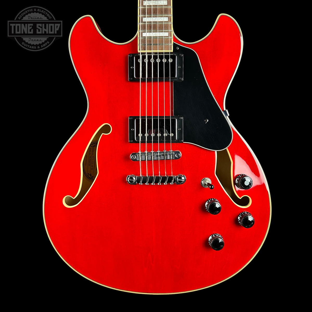 A bright red electric guitar with a black pickguard and chrome hardware, shown against a solid black background. A Tone Shop watermark is visible in the top-left corner.
