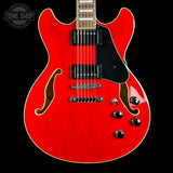 A bright red electric guitar with a black pickguard and chrome hardware, shown against a solid black background. A Tone Shop watermark is visible in the top-left corner.