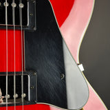 Close-up of a red electric guitar body showing the glossy red finish, black pickguard, pickups, and white binding edge against a dark gray background.