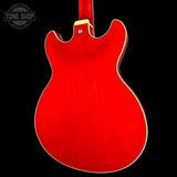 The back of a red electric guitar body with a glossy finish, featuring a cream-colored binding edge and a gold-toned screw, set against a solid black background.