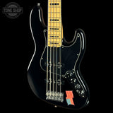 A black electric bass guitar with a maple neck, chrome hardware, and a small American flag decal on the lower bout, shown against a black background with a Tone Shop watermark in the top left.