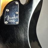 Close-up of a black Fender electric guitar body showing the glossy black pickguard with silver screws and the silver Fender logo.