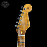 Close-up of a Fender electric guitar headstock in a natural wood finish, showing six tuning pegs and the Fender logo, set against a solid black background.