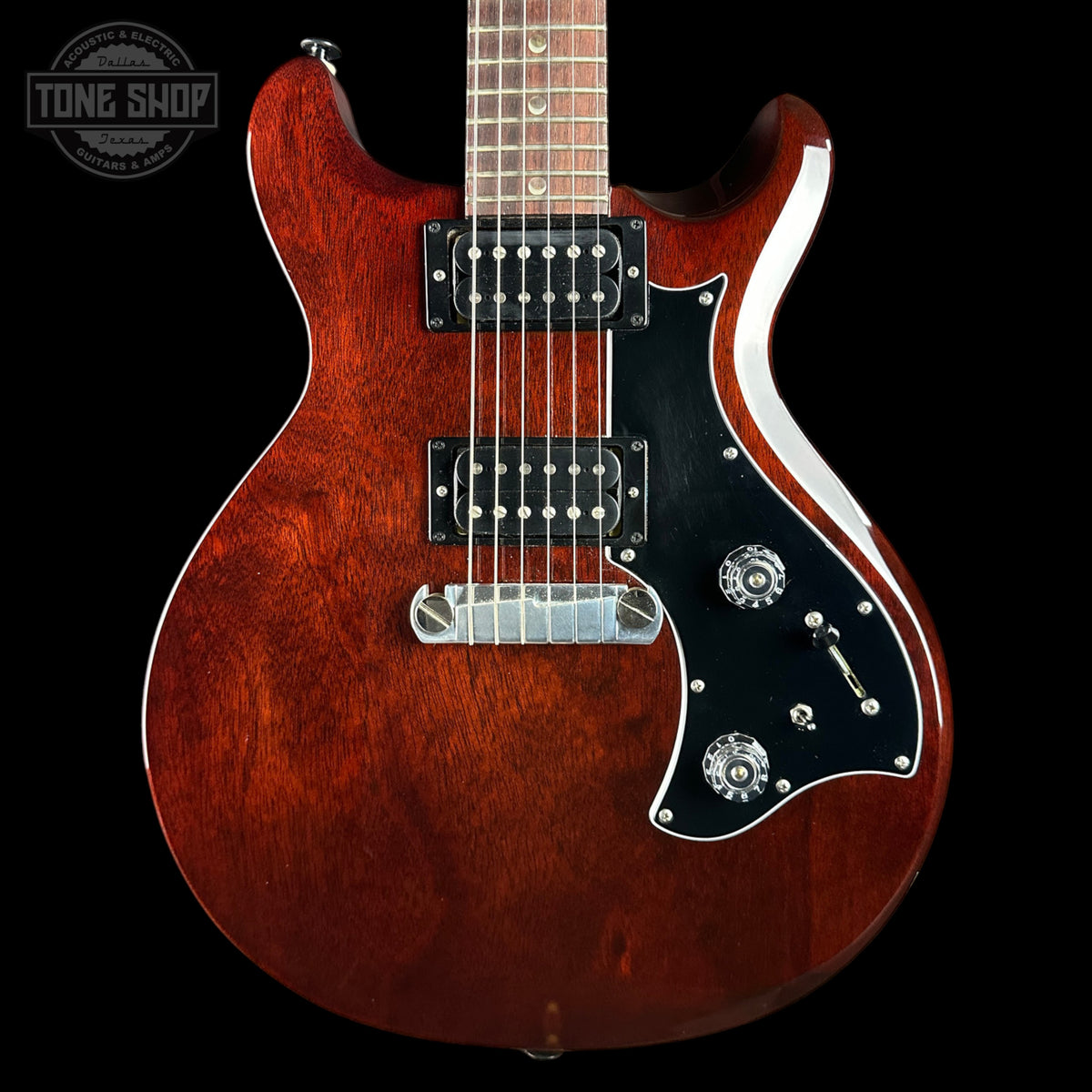 A classic double-cutaway electric guitar with a glossy reddish-brown sunburst finish, black pickguard, and chrome hardware, shown against a solid black background.