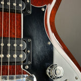 Close-up of an electric guitar body showing a glossy reddish-brown wood finish, black pickguard, chrome hardware, and part of a silver control knob.