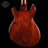Close-up of the back of an electric guitar showing a glossy reddish-brown wood finish with prominent grain patterns, set against a solid black background.