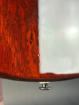 Close-up of a glossy reddish-brown wooden surface with a vertical white section and a small metallic knob at the bottom, photographed against a soft gray background.