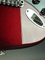 Close-up of a red glitter-finish electric guitar body with chrome hardware, including a bridge, tuners, and a glossy finish reflection.